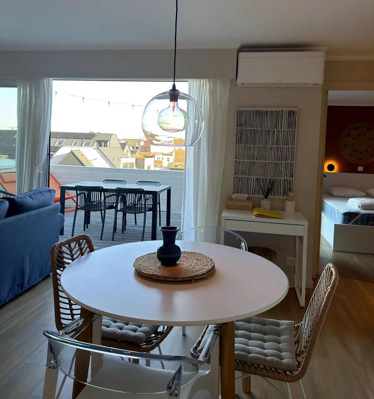 Table ronde pour quatre devant la baie vitrée, terrasse et toits de Blankenberge en toile de fond