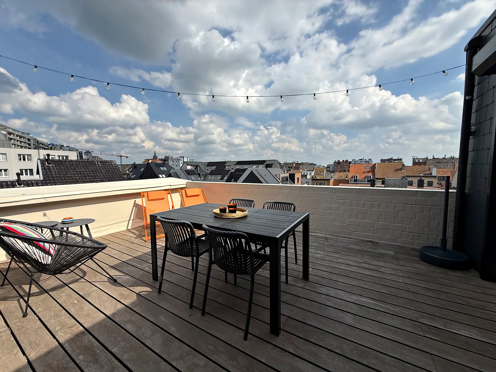 La terrasse en bois sous les guirlandes, avec la table pour quatre et les transats