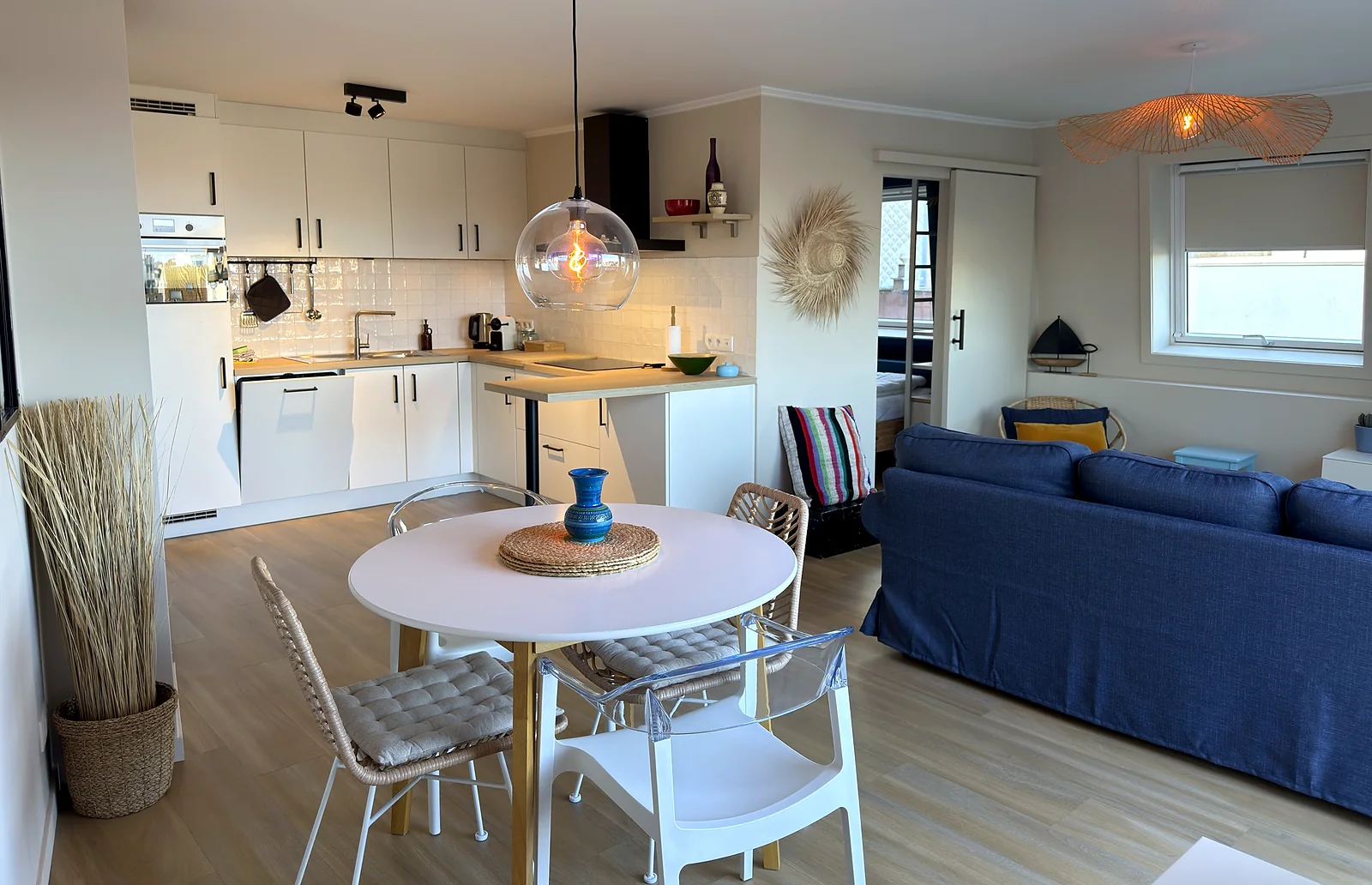 Cuisine équipée ouverte sur le séjour, avec table ronde et canapé bleu